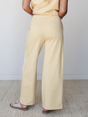 Shot from behind, a model wears soft butter-yellow wide-leg pants with a matching top — the kind of effortless set that makes a Tuesday feel intentional.