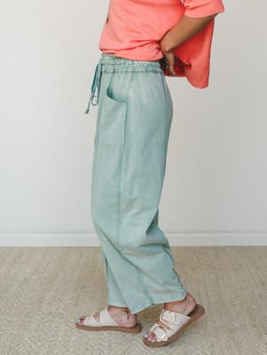 A side-profile shot of wide-leg jade green pants with a smocked drawstring waist, paired with a coral cropped tee and white buckle sandals — easy, colorful, and the kind of outfit that makes a Tuesday feel intentional.