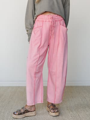 Relaxed barrel-leg pants in a washed dusty pink with visible contrast seaming and a smocked drawstring waist, styled with an oversized olive sweater and platform espadrille sandals for an effortlessly lived-in look.