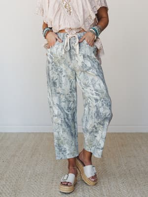 Wide-leg drawstring pants in a soft botanical leaf print styled with a lace-trim crop top, stacked turquoise bracelets, and espadrille wedge sandals — the kind of outfit that feels effortless but clearly wasn't an accident.