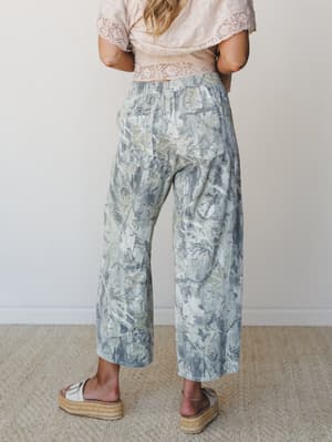 Shot from behind, a model wears wide-leg printed pants in a soft botanical leaf print paired with a blush lace-trim crop top and platform espadrille sandals — earthy, relaxed, and quietly expressive.