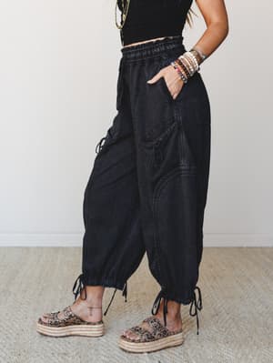 Washed black barrel-leg pants with a smocked waistband and tie ankle cuffs, styled with a black crop top, stacked bracelets, and leopard print platform sandals — the kind of outfit that looks effortless but has clearly been thought about.