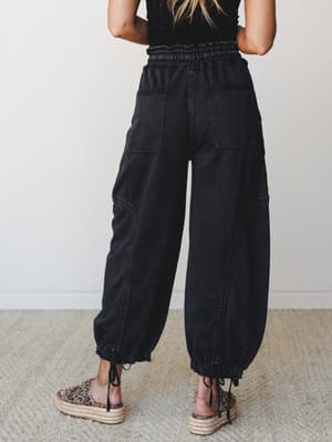 Shot from behind, these washed black wide-leg denim pants with a smocked waist and drawstring ankle cuffs have that effortless, lived-in quality — paired with leopard print platform espadrilles for a look that's relaxed but clearly thought through.