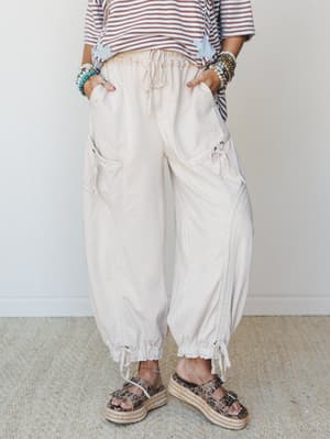 A cropped mid-shot focusing on roomy, oat-colored cargo-style jogger pants styled with a striped tee, stacked beaded bracelets, and leopard print platform sandals — relaxed and expressive without trying too hard.