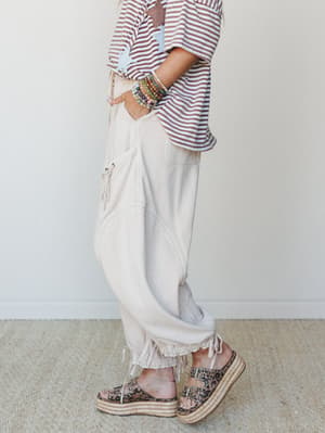 A side-profile shot of relaxed oat-colored barrel pants styled with a rust striped star-patch tee, stacked beaded bracelets, and leopard print platform espadrilles — the kind of outfit that looks like it came together effortlessly but clearly didn't