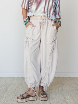 Relaxed harem-style cargo pants in a soft oat tone styled with a striped tee, stacked beaded bracelets, and leopard platform sandals — the kind of outfit that looks effortless but is absolutely a whole vibe.