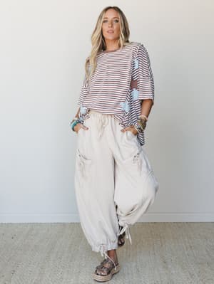 A breezy, relaxed full-body shot of a model in wide-leg oat cargo pants and an oversized striped star-print top — the kind of outfit that looks effortless but is clearly very thought-out.