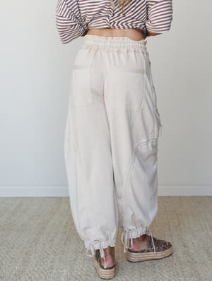 A back-view shot of relaxed, oversized cargo-style jogger pants in a warm oat tone, paired with a striped crop top and leopard platform espadrilles — the kind of outfit that looks effortless but definitely wasn't an accident.
