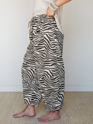 A side-profile shot of wide-leg zebra print pants in cream and brown, styled with a relaxed cream tee and stacked bracelets — the kind of outfit that looks intentional without trying too hard.