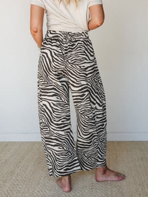 Wide-leg zebra print pants with an elastic waist, styled casually with a tucked cream tee and bare feet — relaxed and a little wild in the best way.