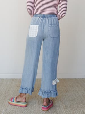Shot from behind, these wide-leg light denim pants with ruffle hems and an eyelet patch pocket feel like the most unexpected thing in your wardrobe — in the best way — styled with a striped long-sleeve and rainbow platform slides for a look that's pl
