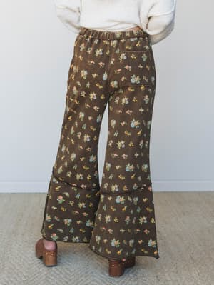 Shot from the back, these wide-leg floral pants in deep olive brown are styled with a cream waffle knit sweater and wood-studded clogs — the kind of outfit that makes a Tuesday feel intentional.