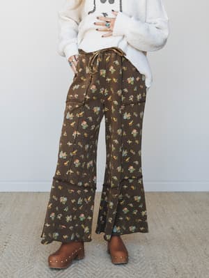 Wide-leg floral pants in deep chocolate brown styled with a chunky cream sweater and wooden clogs — the kind of outfit that feels like a vintage find and a cozy Sunday all at once.