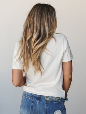 A back-view shot of a model in a soft ivory graphic tee tucked loosely into embroidered denim, the whole look feeling like a good Saturday with nowhere to be.