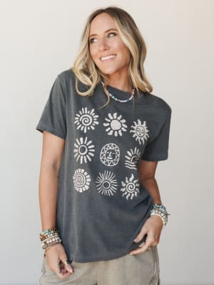 A washed charcoal graphic tee printed with nine sun motifs in a vintage stamp style, styled with layered beaded bracelets and a colorful seed bead necklace — the kind of shirt that makes a Saturday feel intentional.