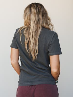 A back-view shot of a worn-in acid-wash graphic tee in deep charcoal, paired with burgundy pants — the kind of effortless combo that looks like it happened on purpose.