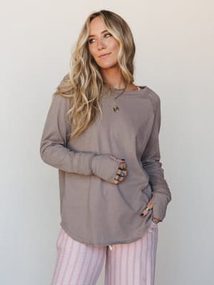 A relaxed, lived-in long sleeve top in warm taupe styled with pink striped pants and layered gold and turquoise jewelry — the kind of outfit that looks effortless at 9am and still feels intentional by noon.