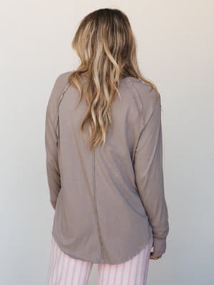 A back view of a relaxed long-sleeve top in warm taupe, styled with pink stripe pants — soft, lived-in, and the kind of thing you reach for without thinking.
