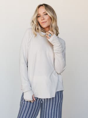 A relaxed, oversized long sleeve top in warm sand beige styled with navy striped wide-leg pants — the kind of effortlessly soft outfit that makes staying in feel just as intentional as going out.