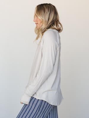 A side-profile shot of a model in a relaxed, sand beige long sleeve top paired with a navy striped bottom — the kind of effortless everyday combo that just works without trying.