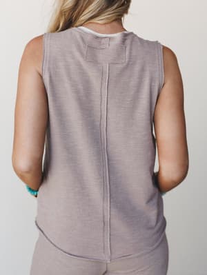 A back-view shot of a soft mauve-taupe sleeveless tank with exposed seam detailing and a tab at the neckline, styled with matching bottoms and turquoise bead bracelets — relaxed and quietly put-together.