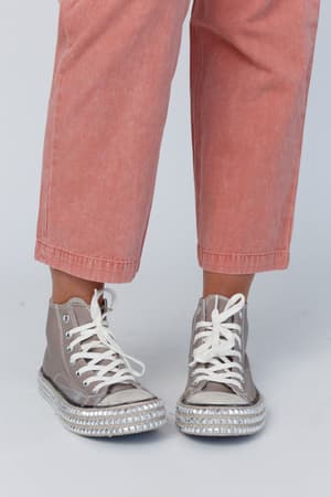 Someone wearing the Chantel Studded High Top Sneaker in Mocha with thick soles and white laces, paired with cropped, faded pink pants, stands against a plain light background.