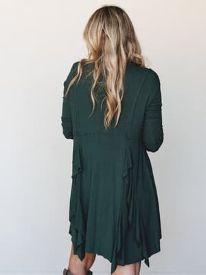 Shot from the back, a flowy hunter green mini dress with long sleeves and cascading ruffle panels shows off its relaxed, lived-in silhouette — the kind of dress that feels as good as it looks.