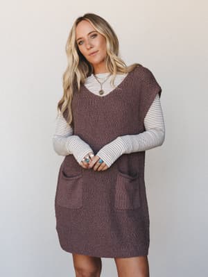 A chunky knit sweater vest dress in mocha layered over a striped long-sleeve tee — the kind of effortless fall outfit that feels intentional without trying too hard, finished with stacked silver and turquoise rings and a gold layered necklace.