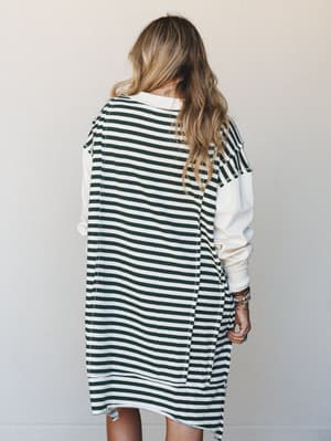 Shot from behind, a model wears an oversized striped midi dress with contrast cream long sleeves — relaxed, effortless, and stacked with colorful beaded bracelets that give it just enough personality.
