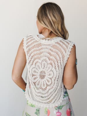 Shot from behind, a model shows off the intricate medallion crochet back of a cream knit vest layered over a light top, paired with a botanical-print bottom — the kind of piece that makes people ask where you got it.