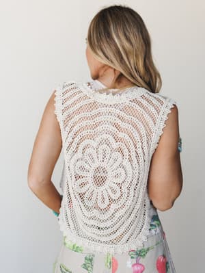 Shot from behind, a model shows off the intricate medallion crochet back of a cream knit vest layered over a light top, paired with a botanical-print bottom — the kind of piece that makes people ask where you got it.
