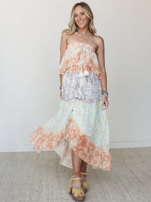 A tiered strapless maxi dress in color-blocked floral panels — coral, lavender, and mint — worn with yellow platform sandals and stacked bracelets, giving off effortless warm-weather energy.