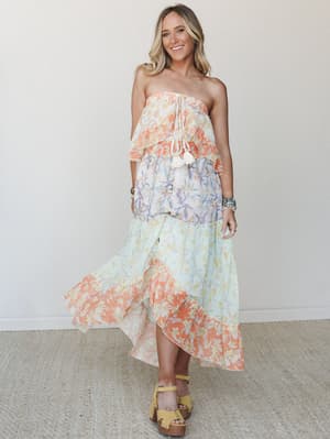 A tiered strapless maxi dress in color-blocked floral panels — coral, lavender, and mint — worn with yellow platform sandals and stacked bracelets, giving off effortless warm-weather energy.