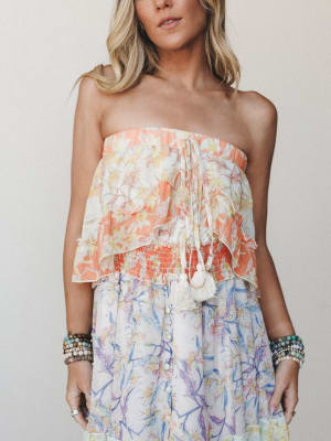 A cropped mid-shot of a floral strapless dress with a ruffled, tiered bodice in warm peach and a flowing skirt in soft lavender-blue — layered with stacked beaded bracelets for that effortless, collected boho feel.