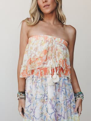 A cropped mid-shot of a floral strapless dress with a ruffled, tiered bodice in warm peach and a flowing skirt in soft lavender-blue — layered with stacked beaded bracelets for that effortless, collected boho feel.