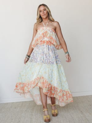 A flowy halter maxi dress in a color-blocked floral print moves through tiers of coral, lavender, and mint — styled with stacked bracelets and wood-platform sandals for a look that feels like a summer afternoon you don't want to end.