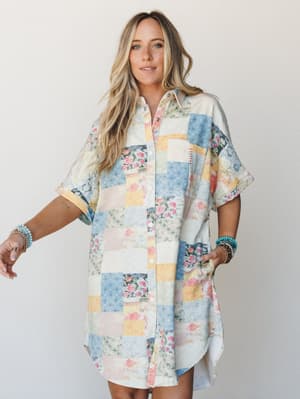 A relaxed, oversized shirt dress in a patchwork print — soft blues, blush, and butter yellow pieced together like a vintage quilt — styled with stacked turquoise bracelets for that effortlessly boho feel.