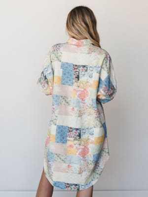 A relaxed shirt dress in a soft patchwork print — florals, paisleys, and geometric blocks in dusty blues, blush, and butter yellow — shown from the back on a model, with the easy, lived-in feel of something you'd find at a vintage market and never le