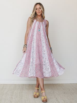 A flowy midi dress with alternating ditsy floral and vertical lace panels catches mid-movement, styled with yellow platform clogs and layered boho jewelry for a look that feels equal parts vintage garden party and free-spirited afternoon.