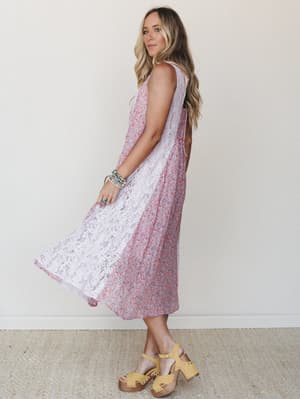 A flowy midi dress with a ditsy floral print and a wide lace panel running down the front catches mid-movement, styled with stacked boho bracelets and yellow platform clogs for a sweet, lived-in summer feel.