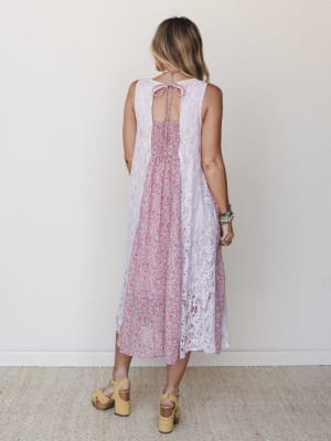 A back-facing shot of a midi dress that layers soft lilac lace panels over a ditsy floral print center, styled with yellow platform clogs and stacked boho bracelets — effortlessly romantic with a vintage-garden feel.