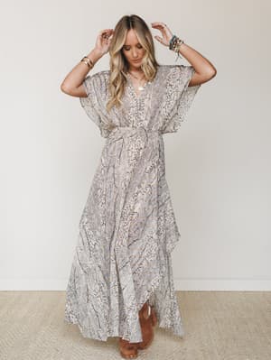 A flowy printed maxi dress with dramatic butterfly sleeves and a ruffle hem, styled with stacked bracelets and suede heels against a clean studio backdrop — effortlessly boho and just dressy enough.