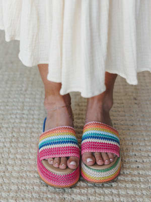 A close-up of rainbow-striped crochet platform slides paired with a flowy cream midi skirt and a delicate anklet — the kind of shoes that do all the talking.