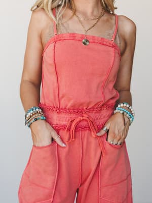 A washed coral jumpsuit styled with layered beaded bracelets and gold chain necklaces — the kind of outfit that looks effortless but clearly wasn't an accident.