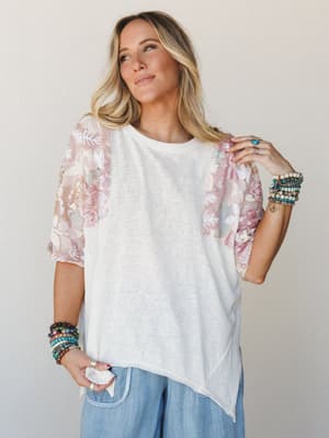 A relaxed oversized tee with sheer floral sequin sleeves worn with wide-leg chambray pants and stacked boho bracelets — the kind of top that makes a casual outfit feel like it has a little secret.