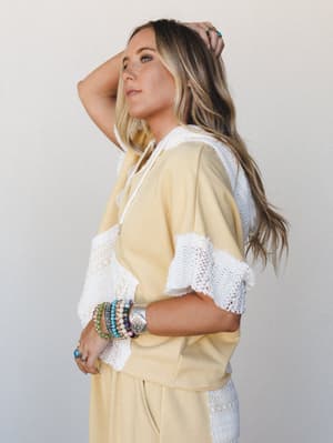 A sun-warmed butter yellow hoodie top with white crochet trim details is styled with matching wide-leg pants, layered boho bracelets, and turquoise rings — the kind of set that feels like a really good Saturday.