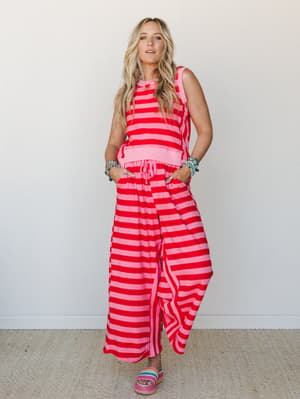 A bold pink-and-red striped matching set — cropped tank and wide-leg pants — styled with colorful stacked bracelets and platform slides, shot clean against a white wall with an effortlessly put-together, summer-ready feel.