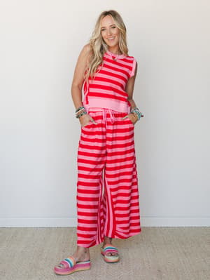 A matching striped two-piece set in bold pink and red worn with rainbow platform slides and stacked bead bracelets — playful and full of personality, the kind of outfit that makes a Tuesday feel like a reason to go somewhere.
