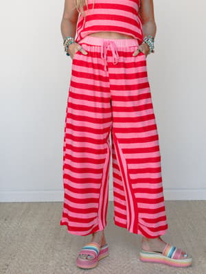 A bold red and pink striped wide-leg pant styled as a matching set with a coordinating crop top, accessorized with stacked bracelets and rainbow platform sandals — playful, confident, and very much the kind of outfit that makes people ask where you g