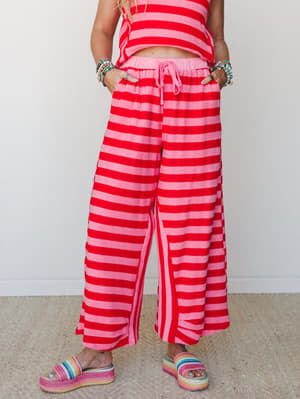A bold pink and red striped wide-leg pant and matching crop top set, styled with rainbow platform sandals and stacked beaded bracelets — the kind of outfit that makes a Tuesday feel like a vacation.